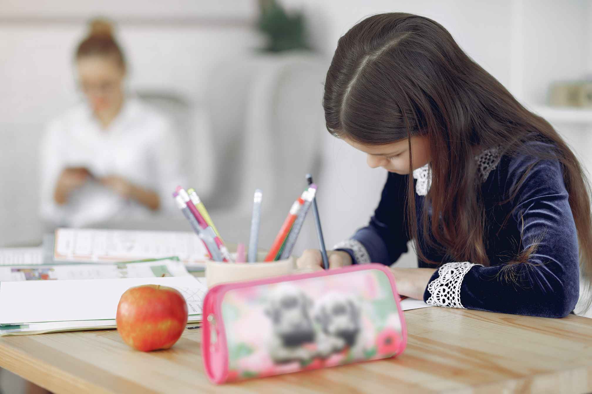 Little girl studying at table near mother in living room